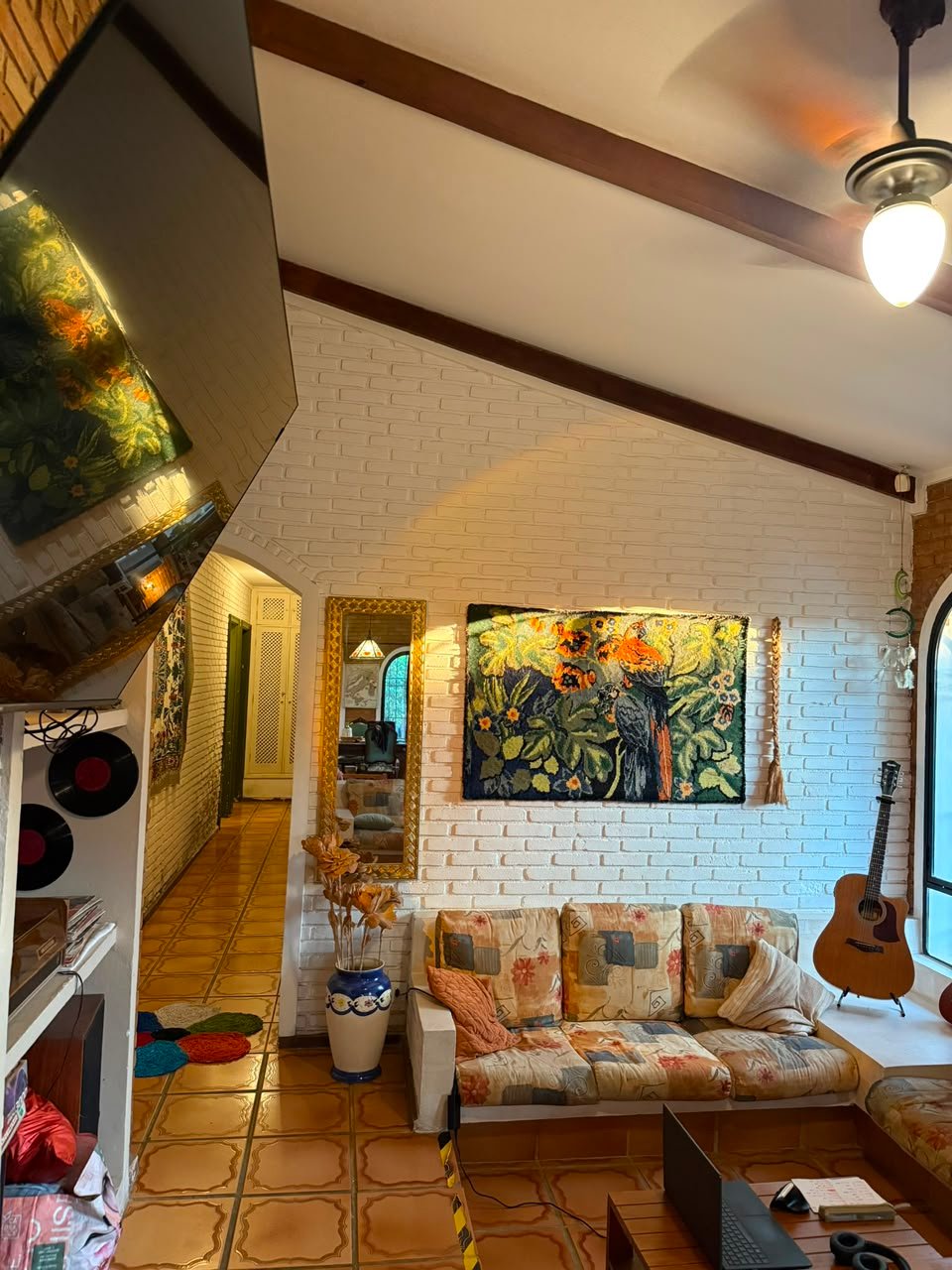 Sala de estar acolhedora da Golden Garden House, com tapeçaria de araras, violão e decoração internacional